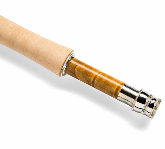 Close-up of a wooden fly fishing rod blank showing the cork handle transition, polished wood shaft, and silver metal tip on a white background.